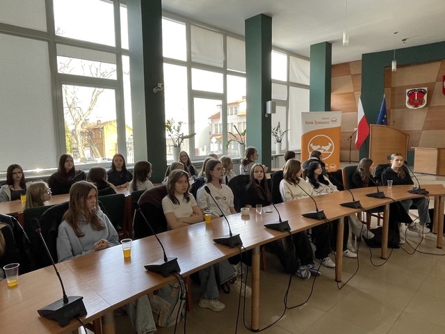 4-_Siedzący_przy_zaokrąglonych_stołach_wolontariusze_po_prawej_stronie_baner_zbiórki_zywności-_Easy-Resize-com