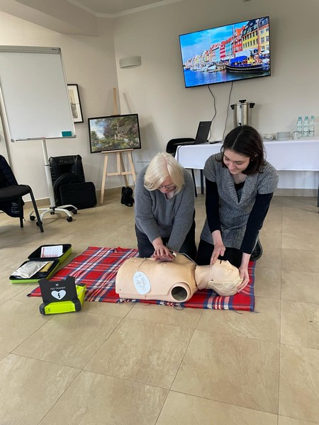 Na kocu leży fantom za nim dwie kobiety klęczą przeprowadzając ćwiczenia resuscytacyjne