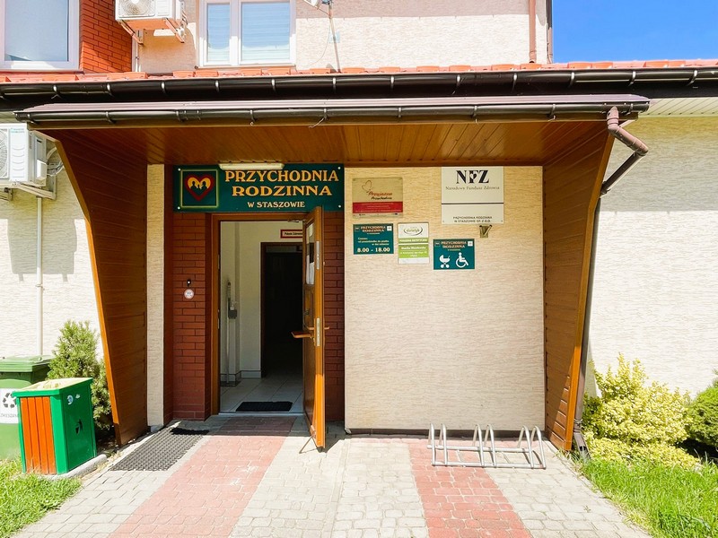 Wejście główne do przychodni z otwartymi na oścież drzwiami, brązowe drzwi pod brązowym daszkiem. Przychodnia rodzinna w Staszowie