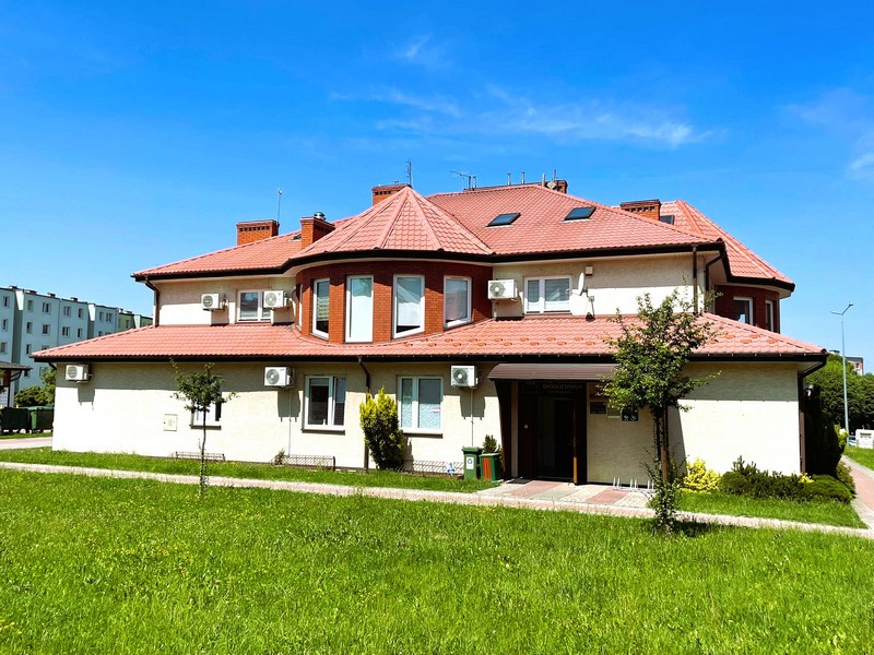 Na zdjęciu widać całość budynku. Kremowy budynek z brązowym dachem. Przychodnia rodzinna w Staszowie