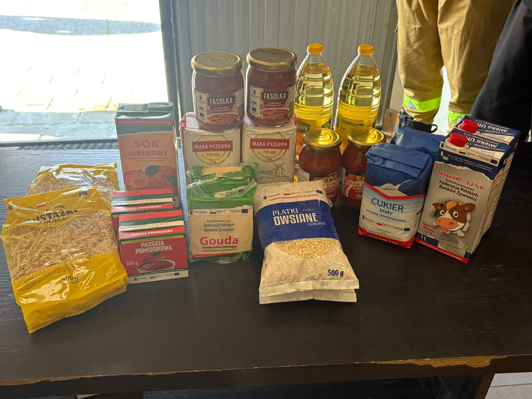 5. Na zdjęciu produkty żywnościowe takie jak olej, makaron, mąka, cukier, mleko, płatki owsiane, ser, sok jabłkowy, passata pomidorowa, fasolka,sos.